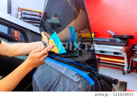 Technician carefully applies window tint film to car door in well it auto workshop using squeegee. 121029852