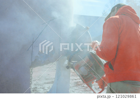 Worker skillfully operates concrete saw, cutting through drainage system well while dust fills air at construction site 121029861
