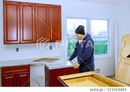 Contractor is carefully placing countertop in newly renovated kitchen with wooden cabinets during construction 121029865