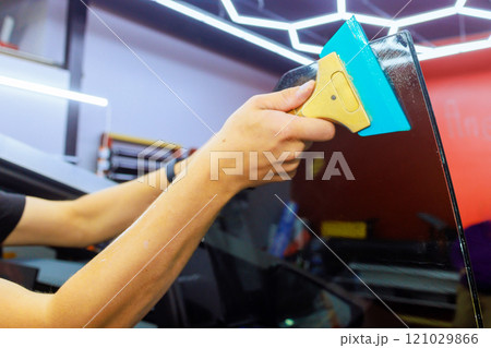 Technician applies tinted film to car window using squeegee in an auto shop. Technician applies tinted film to car window using squeegee in an auto shop. 121029866