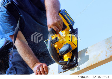 Skilled worker operates circular saw, cutting wood frame on under construction project at work area 121029893