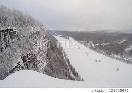 A rocky snow-covered cliff above a frozen river. A rocky snow-covered cliff above a frozen river. 121030475