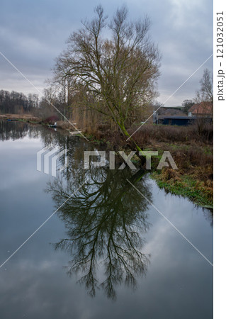 A tree gives a beautiful reflection in a river. A dark sky with clouds in the background A tree gives a beautiful reflection in a river. A dark sky with clouds in the background 121032051