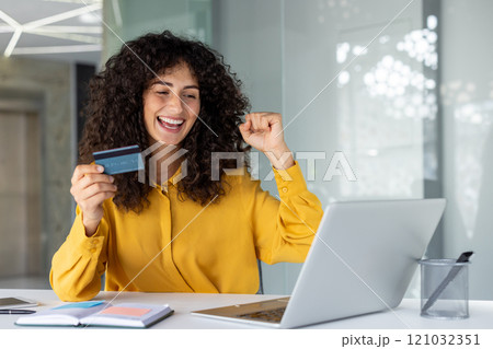 Happy woman in office celebrates successful online shopping with credit card and laptop. She shows excitement and success in financial transaction, symbolizing digital freedom and happiness. Happy woman in office celebrates successful online shopping with credit card and laptop. She shows excitement and success in financial transaction, symbolizing digital freedom and happiness. 121032351
