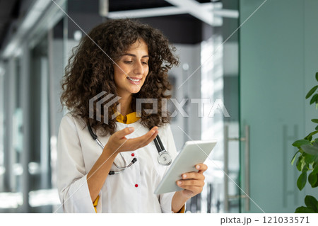 Healthcare professional with curly hair using tablet for video call in modern office. Focused on digital communication, remote consultation, technology, healthcare innovation. Healthcare professional with curly hair using tablet for video call in modern office. Focused on digital communication, remote consultation, technology, healthcare innovation. 121033571