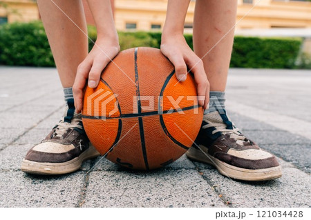A teenage boy holds a ball with his feet after playing basketball. 121034428