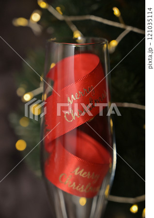 Christmas decor, close-up transparent glass with a red ribbon inside, tree with lights, dark background Christmas decor, close-up transparent glass with a red ribbon inside, tree with lights, dark background 121035114