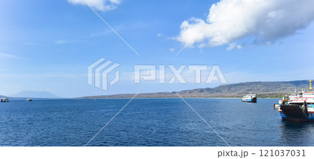 A serene view of the Bali Sea with calm blue waters, distant mountains, and scattered boats under a clear sky. A serene view of the Bali Sea with calm blue waters, distant mountains, and scattered boats under a clear sky. 121037031