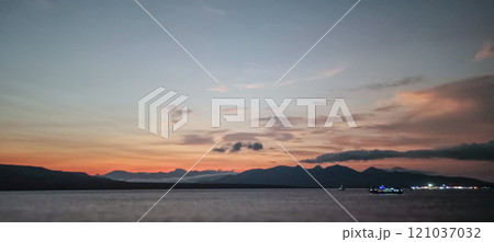A tranquil scene of the sea at dawn with soft hues of orange and blue blending over distant mountains and a calm horizon. A tranquil scene of the sea at dawn with soft hues of orange and blue blending over distant mountains and a calm horizon. 121037032