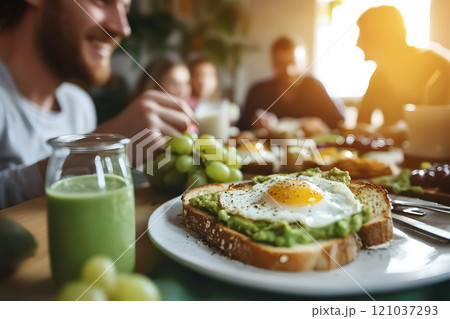 Friends engage in lively conversation over a delightful brunch spread, featuring creamy avocado toast with a sunny-side-up egg, fresh fruits, and nutritious smoothies. 121037293
