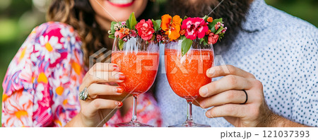 A joyful couple raises their glasses filled with bright, fruity cocktails adorned with fresh flowers. 121037393