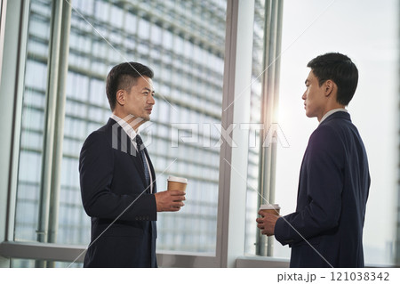 two asian business men standing and talking by the window in office 121038342