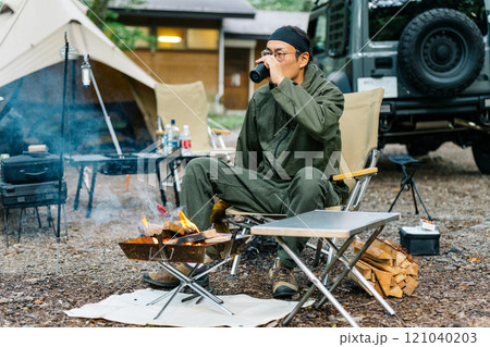 キャンプ場で焚き火する男性キャンパー(飲酒・お酒・焚き火台・ソロキャンプ・ソロキャン) キャンプ場で焚き火する男性キャンパー(飲酒・お酒・焚き火台・ソロキャンプ・ソロキャン) 121040203