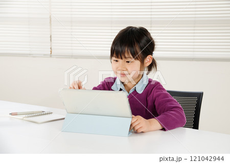 集中してタブレットを操作しながら勉強している小学生の女の子 集中してタブレットを操作しながら勉強している小学生の女の子 121042944