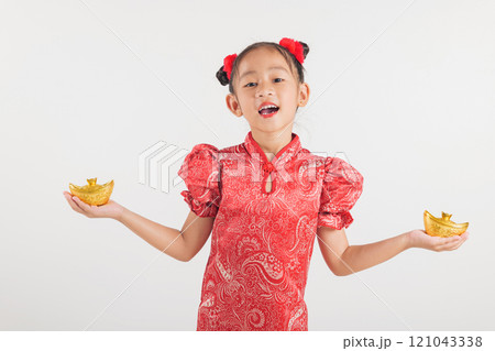 Happy Chinese New Year Smiling Asian girl wearing a red cheongsam dress holds a gold ingot, symbolizing wealth and prosperity. Isolated on a white background, festive and traditional 121043338