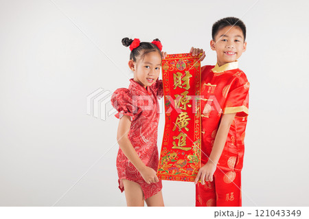 Smiling boy and girl in red qipao dresses hold "FU" couplets to celebrate Chinese New Year. This joyful portrait highlights blessings, prosperity, and cultural heritage. Isolated on white background 121043349