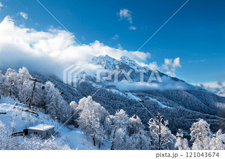 Snowy peaks of mountains above the clouds and gondola lift on a clear winter day 121043674