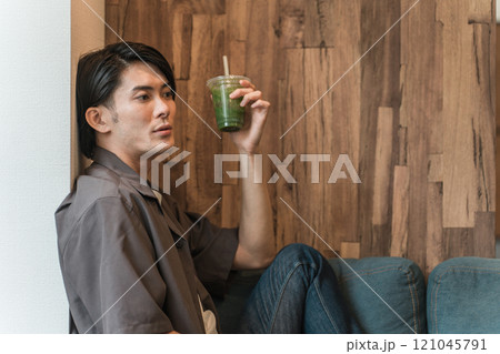 家のソファでグリーンスムージー・青汁・野菜ジュースを飲んでファスティング・断食・ダイエットする男性 家のソファでグリーンスムージー・青汁・野菜ジュースを飲んでファスティング・断食・ダイエットする男性 121045791