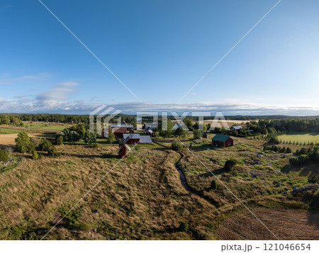Tranquil charm of Aland Islands, Finland. Red farmhouses amidst fields and meadows framing a rustic windmill under a clear blue sky 121046654