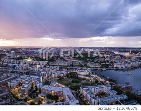 Urban beauty and tranquility of Stockholm with illuminated buildings, parks, and waterways under a dramatic cloudy sky at dusk, seen from an aerial perspective Urban beauty and tranquility of Stockholm with illuminated buildings, parks, and waterways under a dramatic cloudy sky at dusk, seen from an aerial perspective 121046679