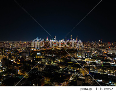 Aerial view of Queens district, with East River, Queensboro Bridge, and Manhattan illuminated skyline of New York City shining brightly at night 121046692