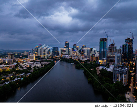 Austin, Texas skyline shining on the waters of Colorado River, creating a breathtaking view as night falls under a dramatic, cloud filled sky 121046821