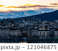 Geneva's cityscape at sunrise features smoking chimneys, waterfront buildings, and Mont Blanc mountain range in the Alps, creating a breathtaking winter scene 121046875