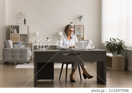 Busy serious senior businesswoman in glasses working at laptop Busy serious senior businesswoman in glasses working at laptop 121047998