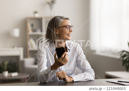 Cheerful grey haired business professional woman in glasses holding cellphone 121048003