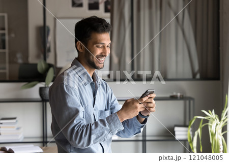 Satisfied Indian businessman using smartphone in office 121048005