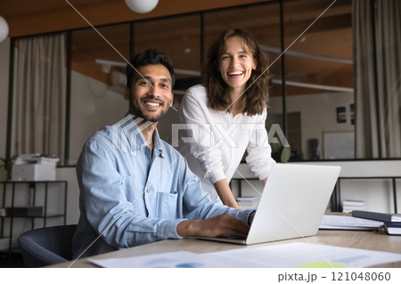 Two workmates posing in modern workplace, laughing, looking at camera 121048060