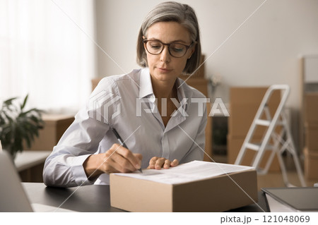 Focused webstore owner woman in glasses managing shipping process Focused webstore owner woman in glasses managing shipping process 121048069