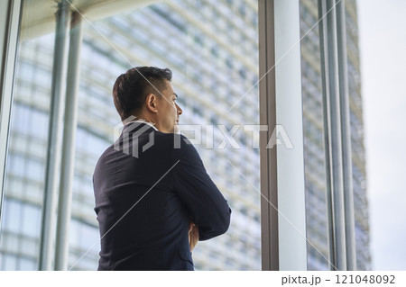 asian businessman standing by window looking at view asian businessman standing by window looking at view 121048092