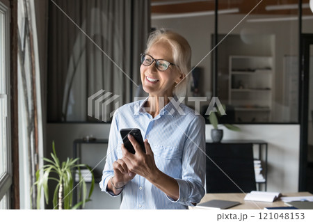 Woman hold smartphone, smile, looks into distance 121048153