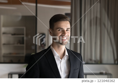 Head shot portrait young businessman posing in modern workspace Head shot portrait young businessman posing in modern workspace 121048162