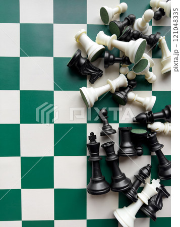 Scattered chess pieces on green and white board in a strategic match Scattered chess pieces on green and white board in a strategic match 121048335
