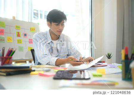 UX designer reviewing mobile application wireframes and color palettes at office desk UX designer reviewing mobile application wireframes and color palettes at office desk 121048636