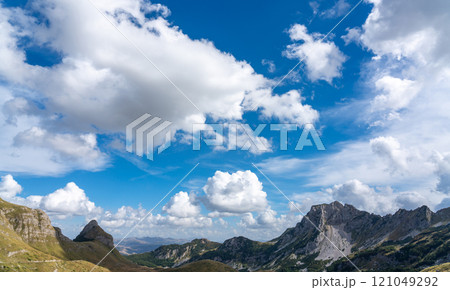 Mountain peaks under a vibrant blue sky with fluffy white clouds. Mountain peaks under a vibrant blue sky with fluffy white clouds. 121049292