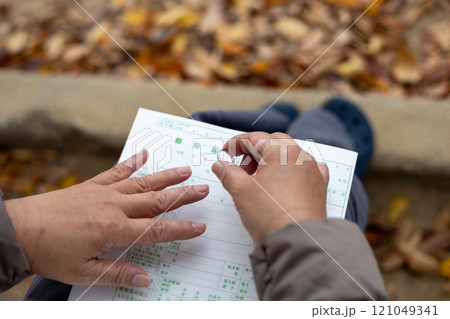 公園のベンチで外した結婚指輪と離婚届を見ている中高年女性 121049341