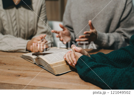 Group of Christians sit together and pray around a wooden table with blurred open Bible pages in their homeroom. Prayer for brothers, faith, hope, 121049502