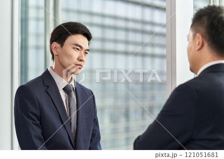 two asian business men standing and talking by the window in office 121051681