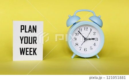 The phrase PLAN YOUR WEEK on a notepad and a yellow background with a clock 121051881