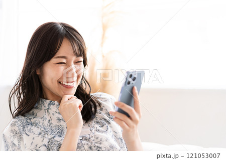 白いソファに座りスマホを持つ黒髪ロングヘアの若い女性 白いソファに座りスマホを持つ黒髪ロングヘアの若い女性 121053007
