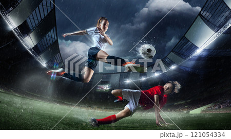 High-action soccer moment featuring female player in white performing powerful kick over player in red. Rainy 3D-modeled stadium. 121054334