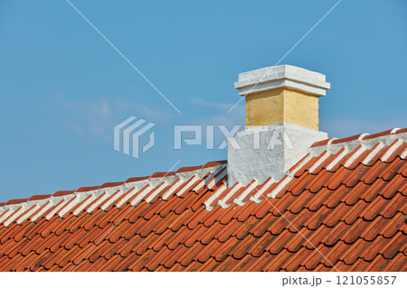 Brick chimney designed on slate roof of house building outside against blue sky background. Construction of exterior architecture of escape chute built on rooftop for fireplace smoke and heat Brick chimney designed on slate roof of house building outside against blue sky background. Construction of exterior architecture of escape chute built on rooftop for fireplace smoke and heat 121055857
