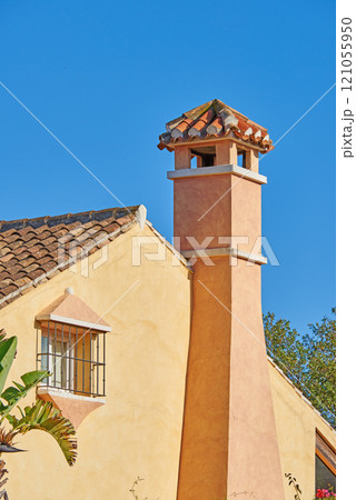 Chimney designed on roof of orange painted house building outside against blue sky background. Construction of exterior architecture of escape chute built on rooftop for fireplace smoke and heat Chimney designed on roof of orange painted house building outside against blue sky background. Construction of exterior architecture of escape chute built on rooftop for fireplace smoke and heat 121055950