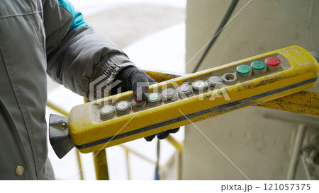 Male hand push remote control switch for overhead crane in the factory, close-up. Electrical control panel of the crane and other lifting equipment in laborer hand. Male hand push remote control switch for overhead crane in the factory, close-up. Electrical control panel of the crane and other lifting equipment in laborer hand. 121057375