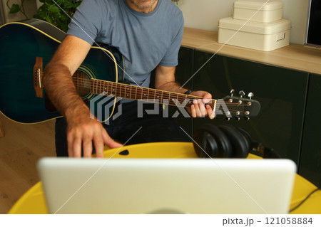 A man sitting in front of the computer practicing online music lessons 121058884