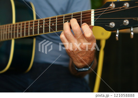 Close-up of a man's hands playing an D chord on acoustic guitar at home Close-up of a man's hands playing an D chord on acoustic guitar at home 121058888