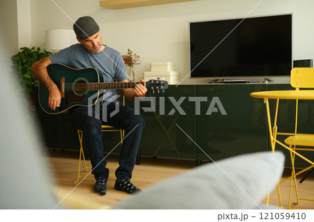 A man sitting at home learning to play a chord on acoustic guitar 121059410